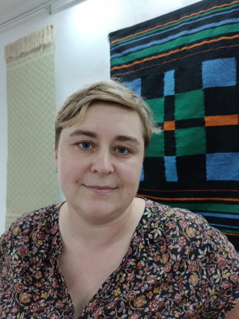 Tkaczka Aleksandra Staszak na pierwszym planie w tle dwie jej prace z motywem Moda na gwiazdki wykonane w technice radziuszka i kilim
