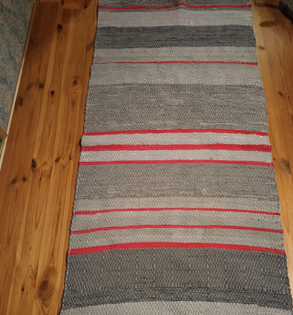 Chodnik tzw. szmaciak autorstwa Urszuli Mendryk. Kolory wątku szare i czerwone szmatki.
